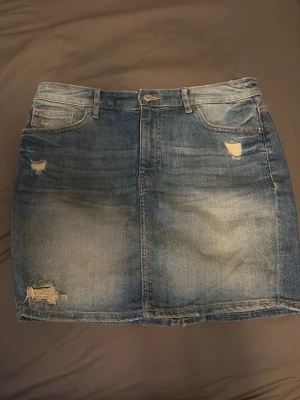 Blå jeanskjol  - blå jeanskjol från H&M. Kjolen har slitna detaljer och råa kanter.