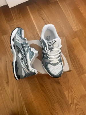 Asics GEL-Kayano 14 White/Grey - Snygga Asics GEL-Kayano 14 sneakers i vitt och grått. Skorna har en sportig design med detaljerad sula och klassisk Asics-logga. Perfekta för dig som gillar streetwear och vill ha bekväma sneakers med modern vibe.