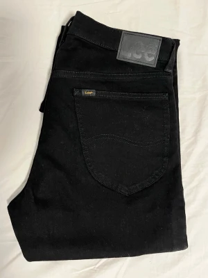 Lee jeans - Snygga svarta jeans från Lee med klassisk rak passform. Jeansen har fem fickor, Lee-logga på bakfickan och patch i midjan. Tillverkade i slitstarkt denimtyg som ger en tidlös look. Perfekta för dig som gillar stilrena och enkla jeans. Aldrig använda eller tvättade, köpta från affären och aldrig haft på dem. Dem är sprillans nya.