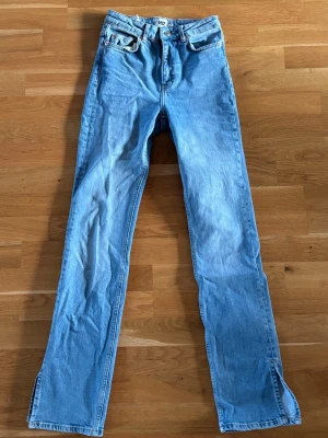 Ljusblå raka jeans med slits - Säljer ett par ljusblå jeans med rak passform och slitsar längst ner vid bensluten. Klassisk femficksmodell med hög midja och dragkedja. Perfekta till en avslappnad och trendig look. Materialet är denim i bomull.