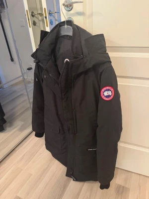 Svart dunjacka från Canada Goose - Säljer en svart Canada Goose jacka med huva och klassisk logotyp på ärmen. Jackan har dragkedja och knappar framtill, flera fickor och ribbade muddar vid ärmsluten. Perfekt för kalla vinterdagar och riktigt varm, varmaste jackan man kan ha! Den är helt ny aldrig använd endast testad. Köptes förra året, kvittot finns😊 storleken är Large men passar även M.