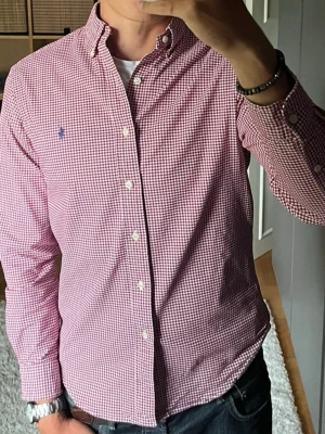 Polo Ralph Lauren oxfordskjorta - stl M - Polo Ralph Lauren oxfordskjorta i rött och vitt, storlek M. Tunt tyg med lite stretch i och knäppbar krage. Slim fit, sitter ganska smal, funkar både nu på sommaren och i höst. Personen på bilden är 189cm, väger 78kg.  Använd men i mycket fint skick, inga hål eller fläckar.  Rök- och djurfritt hem. Skriv gärna om du vill ha fler bilder eller undrar något!