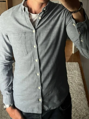 Tiger of Sweden skjorta i gråblå - stl M - Skjorta från Tiger of Sweden, slim fit med button down krage och bröstficka. Funkar året runt till jeans eller chinos. Personen på bilden är 189cm, väger 78kg.   Använd men i mycket fint skick, inga hål eller fläckar.  Rök- och djurfritt hem. Skriv gärna om du vill ha fler bilder eller undrar något!
