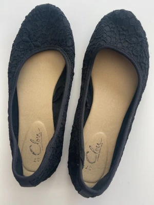 Svarta spetsballerinaskor - Säljer ett par svarta ballerinaskor med elegant spetsdetalj över hela skon. De har rund tå och mjuk innersula för extra komfort. Perfekta för dig som gillar en stilren och feminin look.