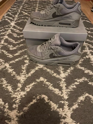 Grå Nike Air Max 90 sneakers - Säljer ett par grå Nike Air Max 90 för att de blev för små, har använt de 2 gånger, ddn har den ikoniska synliga Air-dämpningen i sulan. Swoosh-logga på sidan och detaljer i olika grå nyanser. Skorna tvättas och görs rent innan vi skickar iväg de!
