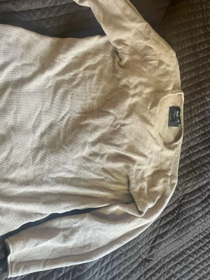Beige långärmad tröja - En stilren beige långärmad tröja med rund halsringning. Tröjan har en diskret struktur i materialet och passar perfekt till en avslappnad look. Enkel att matcha med olika outfits och ett måste i basgarderoben.