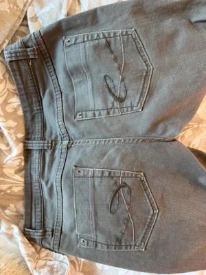 Mörkgrå raka jeans med låg midja - Säljer ett par mörkgrå jeans med rak passform och låg midja. Jeansen har klassiska fem fickor och bälteshällor. Materialet ser ut att vara denim med en lätt tvättad look. Perfekta för en avslappnad och trendig stil. Storlek 36! 