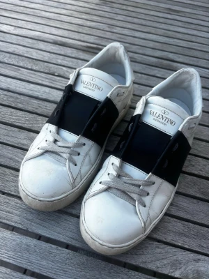Valentino Garavani vita sneakers - Snygga vita sneakers från Valentino Garavani med bred svart rem över mitten och vita skosnören. Storleken är 35,5 men passar även 36❤️