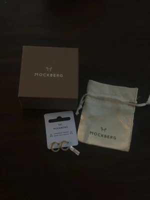 Guldpläterade hoops från Mockberg - Säljer ett par stilrena hoops från Mockberg med klicklås, tillverkade i rostfritt stål och 18k guld PVD-plätering. Örhängena är små, runda och har en klassisk design som passar till allt. Kommer med original ask och tygpåse från Mockberg. Aldrig använda. Nypris 399kr. Går även att hämta upp i centrala Kungälv om så önskas 