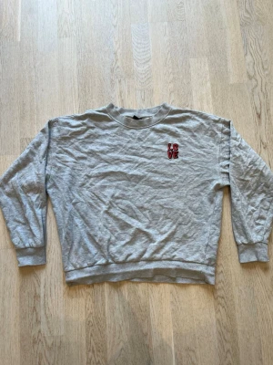 Grå sweatshirt från Gina Tricot - Grå sweatshirt från Gina Tricot med broderad text 'LOVE' i rött och svart på bröstet. Tröjan har rund hals, långa ärmar och ribbade muddar vid ärmslut och nederkant. Perfekt för en avslappnad och trendig look. Tveka inte på att skriva en fråga eller be om fler bilder🌸🌸