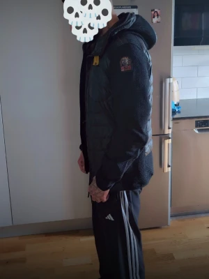 Svart pufferjacka med huva - Säljer en svart pufferjacka med huva och dragkedja framtill. Jackan har quiltade partier och släta ärmar i stickad look. Detaljer som patch på ärmen och gul dragkedjedetalj vid halsen. Perfekt för kalla dagar och riktigt snygg streetstil. Lägger bara upp annonsen igen försöker på nytt  skriv vid intresse  passar medium med 