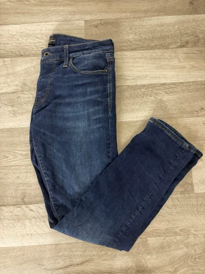 Mörkblå slim fit jeans W32/L32 - Snygga mörkblå jeans i slim fit-modell med klassiska fem fickor och gul kontrastsöm. Jeansen har en lätt tvättad look och är tillverkade i ett stretchigt denimtyg som ger en bekväm passform.