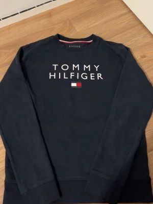 Marinblå sweatshirt Tommy Hilfiger - Snygg marinblå sweatshirt från Tommy Hilfiger med klassisk logga och flagga på bröstet. Tröjan har rund halsringning och långa ärmar. Perfekt för en avslappnad och stilren look.