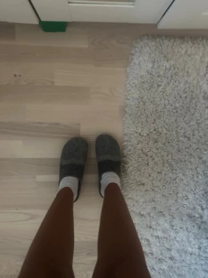 Gråa tofflor i filtmaterial - Mysiga gråa tofflor i filtmaterial med enkel slip-in design. Perfekta för att hålla fötterna varma hemma. Klassisk modell utan synligt märke och neutrala färger som passar till allt. (Vet ej vilket märke det är)
