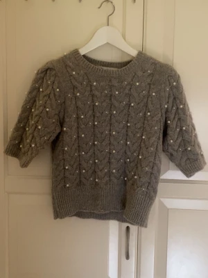 Grå stickad tröja med pärlor - Supersöt grå stickad tröja med korta puffärmar och dekorativa pärlor över hela plagget. Tröjan har ett flätstickat mönster och bred ribbad kant vid ärmslut och nederkant. Säljer då den inte kommer till användning💗Perfekt nu till hösten.🍁