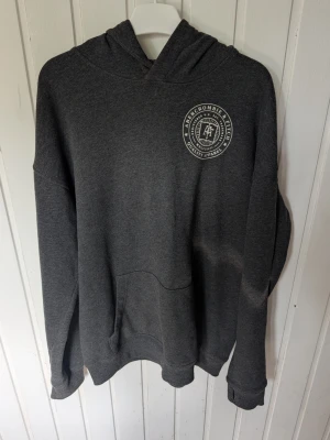 Mörkgrå hoodie Abercrombie Kids - Mörkgrå hoodie från Abercrombie Kids i relaxed fit. Hoodien har en stor ficka framtill, ribbade muddar och en vit logga på bröstet. Tillverkad i mjukt sweatshirtmaterial och har en klassisk huva.