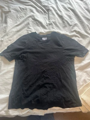 Svart basic t-shirt i bomull - En enkel svart t-shirt med rund hals och korta ärmar. Tillverkad i mjuk bomull som känns skön mot huden. Perfekt att matcha med jeans eller shorts för en clean och stilren look. Ärmarna är puffiga upptill och längst nere på ärmarna är dom lite trängre så det ger puffiga armar.