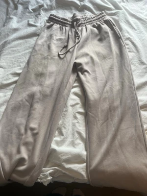 Beige mjukisbyxor med dragsko - Snygga beige mjukisbyxor med resår och dragsko i midjan. Byxorna har raka ben och är gjorda i ett mjukt och bekvämt material, perfekta för en avslappnad stil. Passar dig som gillar enkel och stilren design.