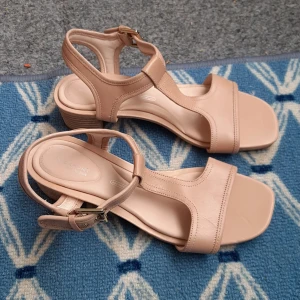 Helt nya.Beige sandaler med klack från Rockport - Säljer ett par stilrena beige sandaler från Rockport med låg klack och justerbart spänne vid ankeln. Skorna har öppen tå och platt sula framtill, perfekt för varmare dagar. Skor är helt nya. 