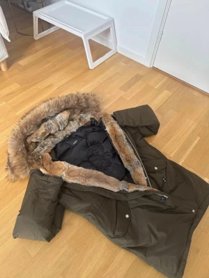 Olivgrön parkas med fuskpäls Hawk lux - Snygg olivgrön parkas med stor huva fodrad med mjuk fuskpäls i bruna och grå toner. Jackan har dragkedja och knappar framtill, stora fickor och en längre passform som håller dig varm under kalla dagar. Perfekt för dig som vill ha både stil och funktion. Äkta päls av både kanin och räv Aldrig anvand och är helt ny Köpte för 5000 kr så säljer därför för minst 2500. Säljer för jag redan köpt ny vinterjacka
