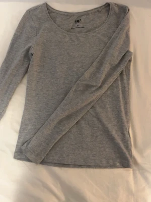 Grå långärmad topp från 157 - En enkel och stilren grå långärmad topp från 157. Tillverkad i mjuk bomullsblandning med rund halsringning och normal passform. Perfekt basplagg att matcha med allt i garderoben.