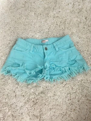  Turkosa shorts - Säljer ett par turkosa/ljusblå jeansshorts med fransig kant och slitna detaljer framtill. Shortsen har klassisk femficksmodell, bälteshällor och knappstängning. Perfekta för sommardagar och ger en avslappnad vibe.🥰pris kan diskuteras  
