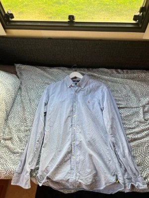 Ljusblå skjorta från Polo Ralph Lauren - Klassisk ljusblå skjorta från Polo Ralph Lauren i slim fit. Skjortan har knappar framtill, button-down krage och den ikoniska broderade loggan på bröstet. Tillverkad i mjuk bomull och passar perfekt till både jeans och chinos.