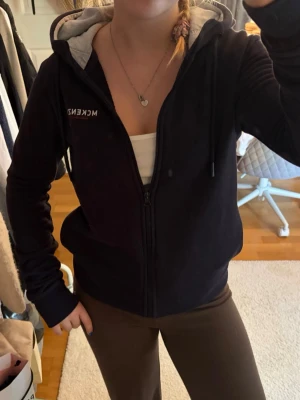 Svart hoodie med dragkedja från McKenzie - Svart hoodie från McKenzie med dragkedja framtill och vit logga på bröstet. Utrustad med huva och grått innerfoder i luvan. Perfekt för chill dagar och enkel att matcha med andra plagg. Klassisk passform och mjukt material. Skriv pm vid funderingar!☺️