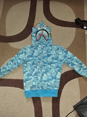 Bape hoodie - Blå hoodie från bape, köpt begagnad+använd av mig ett litet antal gånger men den har inga defekter från vad jag vet, kan alltid dubbelkolla. Strl M men sitter mera åt S hållet