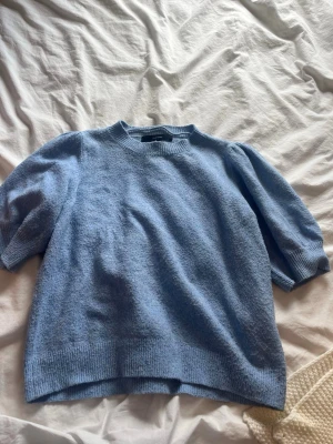 Ljusblå stickad tröja Vero Moda - Ljusblå stickad tröja från Vero Moda med korta puffärmar och ribbade muddar vid hals, ärmslut och nederkant. Tröjan har en mjuk och mysig känsla, perfekt för lager på lager. Enkel och stilren design som passar till mycket. Säljer eftersom den inte kommer till användning.