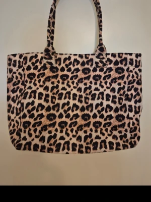 Shoppingväska med leopardmönster - Snygg shoppingväska med leopardmönster i beige, brunt och svart. Väskan har två axelband och ett stort huvudfack med en innerficka som stängs med dragkedja. Knappt använd