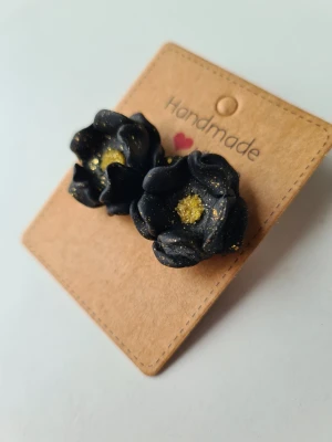 Handgjorda svarta blomörhängen med glitter - Unika handgjorda örhängen i form av svarta blommor med glittrande gulddetaljer. Skulpterade för hand av mig i polymerlera. 