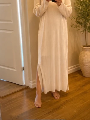 Lång beige klänning med slits - Långärmad beige klänning i ribbat material med rund halsringning och slits på sidan. Klänningen har en rak och loose passform som ger en avslappnad look. Perfekt för dig som gillar minimalistisk stil och mjuka toner.