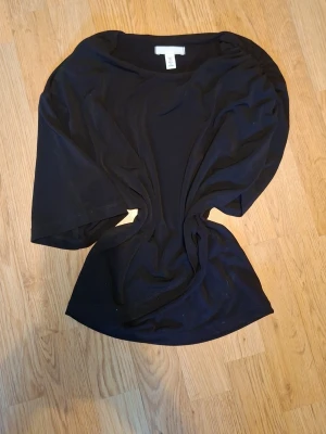 Svart topp med vid ärm - En svart topp med lös passform och breda, halvlånga ärmar. Toppen har rund halsringning och är tillverkad i ett mjukt material som känns bekvämt mot huden. Perfekt att styla med jeans eller kjol för en enkel och snygg look.
