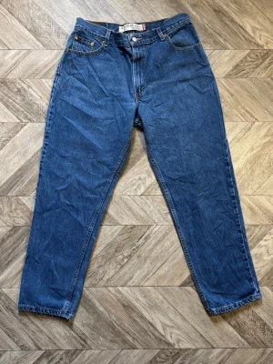 Blåa Levi's 550 - Säljer ett par blå jeans i modellen classic relaxed tapered. Jeansen har fem fickor, knappgylf och raka ben som smalnar av nedtill. Tillverkade i klassisk denim med kontrastsömmar. Perfekta för en avslappnad och stilren look. Längd 99cm Bredd 38cm