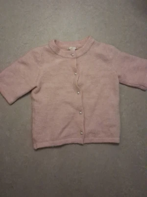 Ljusrosa kofta från Gina Tricot - Söt ljusrosa kofta från Gina Tricot med rund halsringning och pärlknappar framtill. Koftan har halvlånga ärmar och är stickad i ett mjukt material som känns skönt mot huden. Perfekt att slänga över en topp för en chill look.