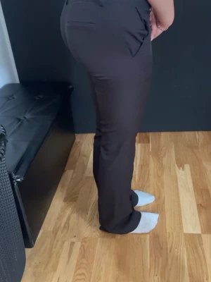 Svarta kostymbyxor lågmidjande - Stilrena svarta kostymbyxor med bootcut-passform och pressveck. Byxorna har fickor bak och stängs med dragkedja och knapp framtill. Materialet ser ut att vara en stretchig och mjuk blandning som ger en snygg siluett.