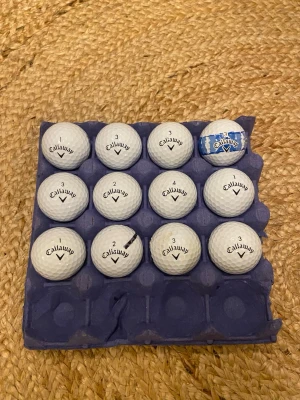 Callaway Supersoft golfbollar 12-pack - Säljer ett 12-pack vita Callaway Supersoft golfbollar. En av bollarna har blått tryck och mönster, resten är klassiskt vita med svart logga. Perfekt för dig som vill fylla på golfbagen med kvalitetsbollar.