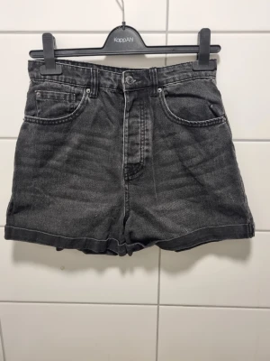 Svarta högmidjade jeansshorts - Snygga svarta högmidjade jeansshorts från Stradivarius. Klassisk femficksmodell med knapp och dragkedja framtill. Shortsen har en avslappnad passform och uppvikta benslut, perfekta för en chill sommarlook.