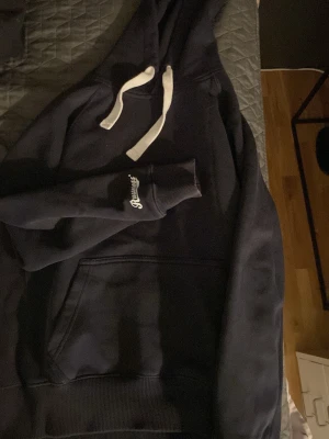 Russemerch - Säljer en mörkblå hoodie med stora vita dragsnören och magficka från russemerch På ärmen finns en liten vit brodyrtext. Hoodien har en klassisk passform och ribbade muddar vid ärmslut och nederkant. Perfekt för en chill och avslappnad stil. Igentligen L men sitter som en M. Aktiv och svarar snabbt