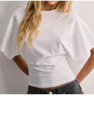 Vit croppad t-shirt med vida ärmar från Nelly  - Säljer en stilren vit t-shirt med croppad passform och vida, korta ärmar. Tillverkad i mjuk bomull som känns skön mot huden. Perfekt till jeans eller kjol för en clean look. Den har aldrig används utan bara legat i garderoben. 
