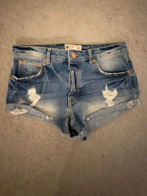Blå jeansshorts - Säljer ett par svin snygga blå jeansshorts med detaljer och uppvikta benslut. Shortsen har klassisk femficksdesign, knappgylf och en cool, avslappnad look. Perfekta för sommardagar och festivaler. Älskar dessa men säljer för att de tyvärr är för stora