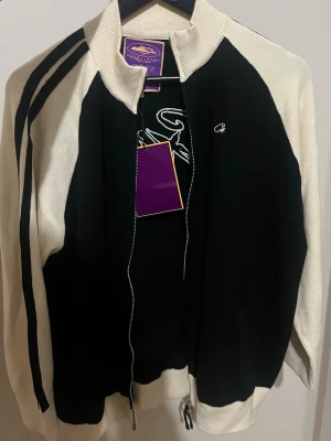 Svartvit finstickad Corteiz ziptröja stl S - Unisex Snygg svartvit corteiz ziptröja med hög krage och kontrasterande vita ärmar. Tröjan har svarta ränder längs ärmarna och en liten broderad logga på bröstet. Tillverkad i mjukt stickat material och har ribbade muddar vid ärmslut och nederkant. Helt ny! 