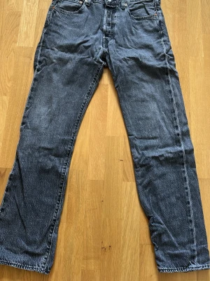 Levi's 501 raka jeans svart W32 L32 - Klassiska svarta Levi's 501 jeans med rak passform. Jeansen har knappgylf och är tillverkade i slitstark denim. Perfekta för en avslappnad och tidlös look.