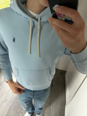 Ljusblå polo Ralph Lauren hoodie  - Snygg och stilren hoodie från Polo Ralph Lauren. Jag är 180 cm / 70 kg och bär storlek S på bilderna, så passformen syns tydligt.  Hoodien är i bra skick, men har tre mindre diskreta fläckar: en längst ner på framsidan, en på ryggen och en på vänster ärm. De är väldigt svåra att se om man inte tittar noggrant, men jag vill självklart vara transparent med detta.  Modell: Polo Ralph Lauren Hoodie Storlek: S Nypris: ca 2 200 kr Skick: Bra skick, mindre diskreta fläckar  Mått:  * Längd: 66 cm * Bred
