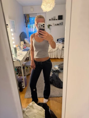 Mörkblå bootcut jeans med låg midja - Säljer ett par mörkblå bootcut jeans med låg midja och klassiska fem fickor. Jeansen har kontrastsömmar och är tillverkade i ett stretchigt denimtyg som sitter snyggt på kroppen. Perfekta för en avslappnad och trendig look. (FLÄCKEN ÄR PÅ SPEGELN EJ BYXAN) storlek 24/32