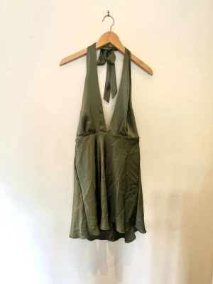 Grön halterneck miniklänning från Zara - Snygg grön halterneck klänning från Zara. Tyvärr har den mindre maskor och defekter i tyget som man ser på bilderna, det är dock ingenting man ser. Jag har använt den och jag har normalt S. Snygg! 