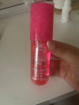 Blossom Veil Body Mist 90ml - Fräsch body mist med doft av orange blossom och gerbera. Flaskan är cylinderformad i genomskinlig plast med rosa vätska och ett stort rosa lock. Perfekt att ha i väskan för en snabb uppfräschning under dagen.