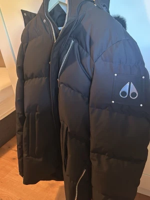 Svart dunjacka från Moose Knuckles - Säljer en svart dunjacka från Moose Knuckles med huva och hög krage. Jackan har en bröstficka med dragkedja, två sidofickor och en patch med logga på ärmen. Perfekt för kalla vinterdagar tack vare det tjocka dunfodret. Jag flyttar till Saudi Arabien om 2 veckor så säljer allt jag inte ska använda o en sån jacka är självmord o ha där. Köpte den på Boozt för 12k kvitto finns o allt finns bara att fråga o snälla inga dumma frågor. Den har sån svart päls oxå.