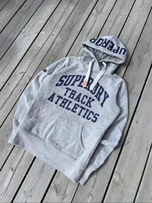 Superdry hoodie grå blå - Snygg grå hoodie med mörkblå text. Den är i bra skick.size s men passar xs